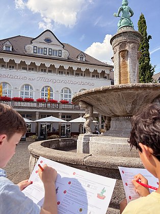 Zwei Kinder stehen mit einer Schatzkarte am Schatzgräberbrunnen auf der Essener Margarethenhöhe