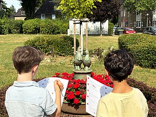 Mit der Schatzkarte über die Margarethenhöhe Zwei Kinder mit Schatzkarten in der Hand stehen vor der von Richard Malin geschaffenen Plastik "Hähnchen und Hühnchen"