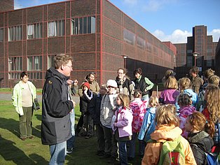 Eine Schulklasse auf dem Gelände der Zeche Zollverein hört draußen dem Gästeführer zu.