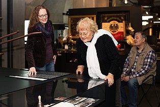 Senior*innen während einer Führung. Im Hintergrund sitzend, im Vordergrund ein Exponat betrachtend.