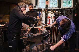 Drei Menschen schmieden während der Schmiedevorführung im Halbachhammer