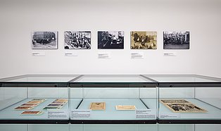 Das Foto gibt einen Einblick in die Ausstellung "Hände weg vom Ruhrgebiet" Die Ruhrbesetzung 1923-1925". Zu sehen ist eine Vitrine mit Exponaten. Darüber hängen fünf Fotografien.