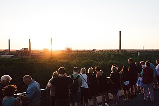 Menschenansammlung betrachtet den Sonnenuntergang auf dem Gelände von Zeche Zollverein.
