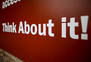Große weiße Buchstaben auf roter Wand mit dem englischen Text ‚Think About it!‘