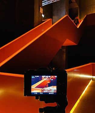 Rot beleuchtetes Treffenhaus im Ruhr Museum. Im Vordergrund steht einen Kamera, die die Szenerie aufnimmt.