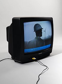 Fotografie von einem Fernseher, der einen Mann vor einer Industrieanlage zeigt.
