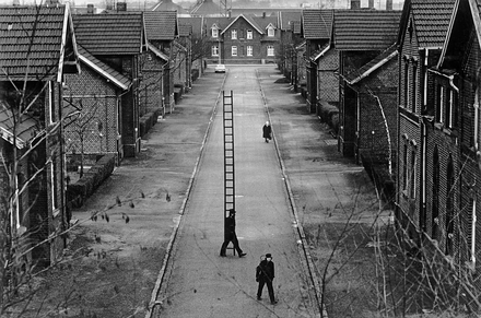 Black and white aerial view of a housing estate with two chimney sweeps walking along the street.